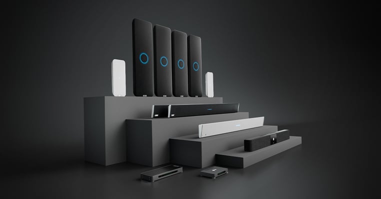 Nureva audio products on a tiered display fixture arranged by room size and use case, from audio conferencing in medium meeting rooms to full-featured audio in extra-large classrooms and boardrooms.