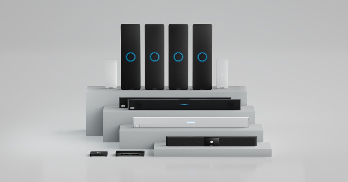 Nureva audio systems arranged on a tiered white platform. Includes an HDX full-featured audio system with four audio bars, two microphone pods and a system hub for equipping large boardrooms. With it are the three HDL audio conferencing systems for a wide range of conference rooms.