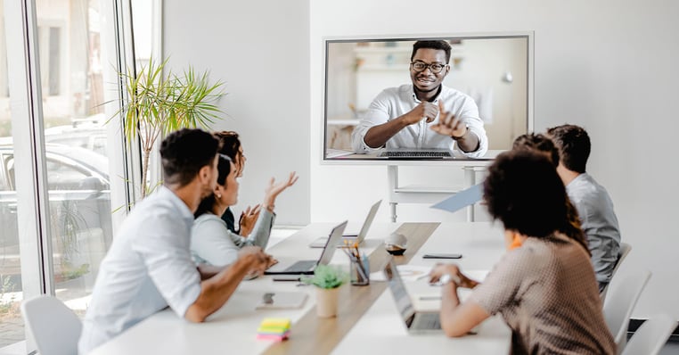 Team in a conference room joining a video meeting on a wall display, illustrating unified communications with integrated audio conferencing for hybrid collaboration.