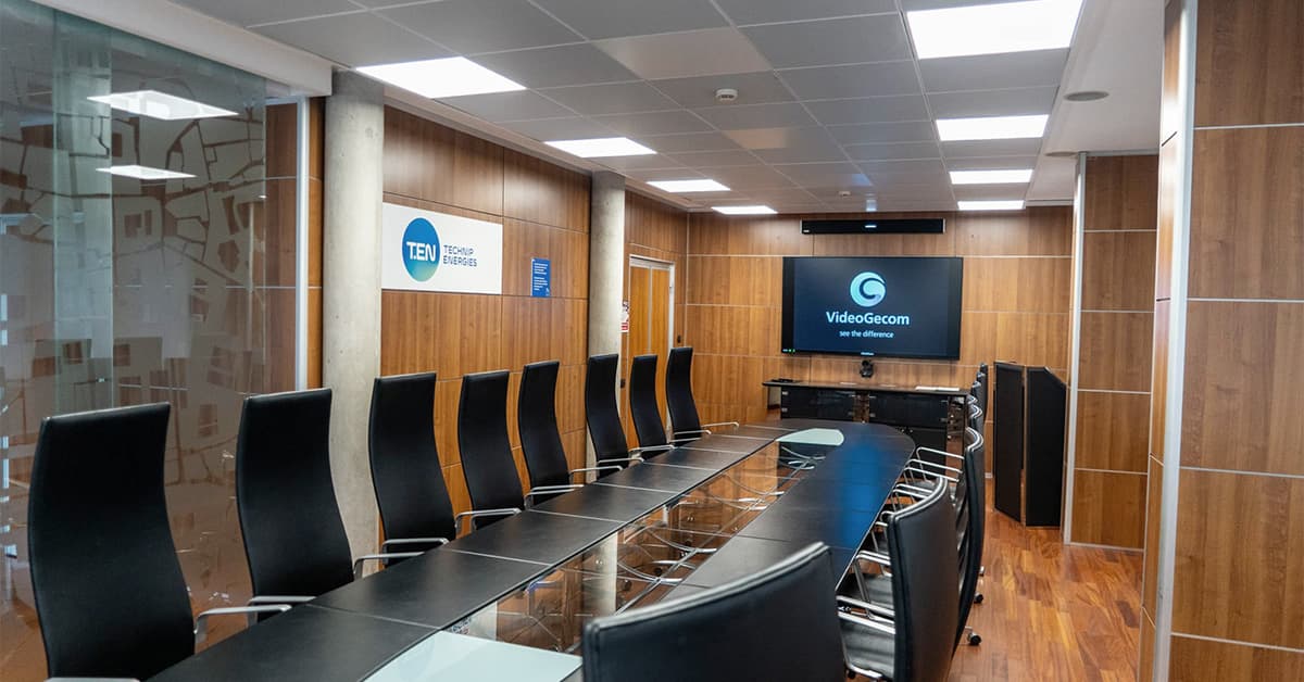 Symmetrical view of a modern boardroom table toward a front display and wall-mounted Nureva HDL310 audio conferencing microphone and speaker bar designed for large-room hybrid collaboration.