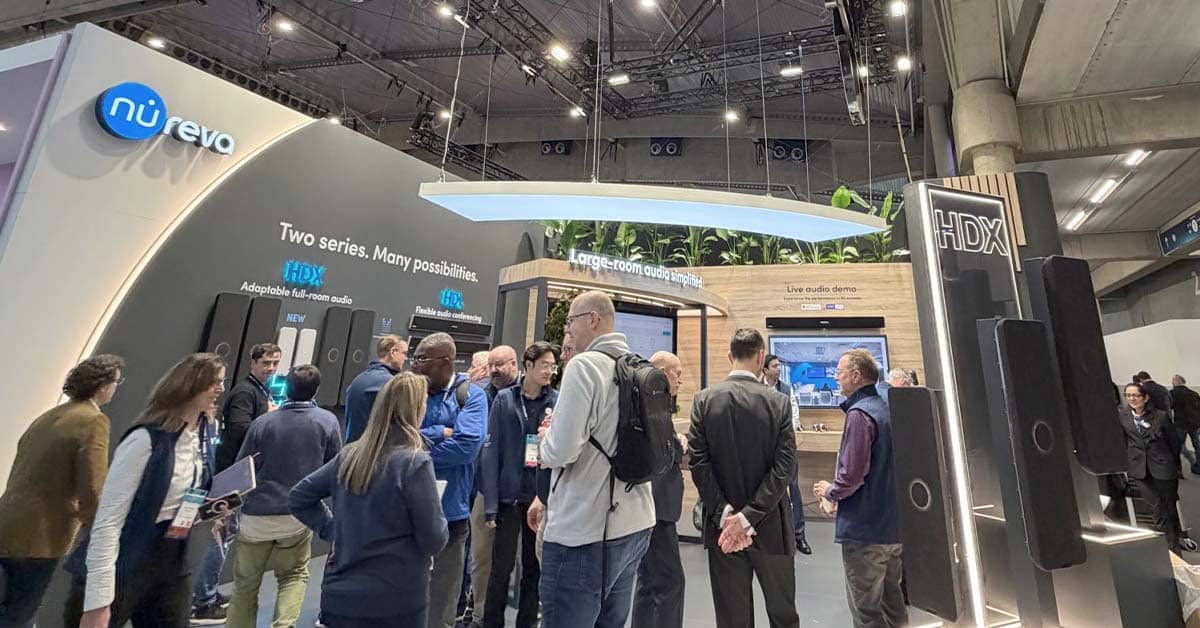 A busy Nureva ISE stand with large displays showcasing HDX and HDL audio systems. Multiple attendees gather around product stations and demonstrations, while overhead signs highlight features like “Large-room audio simplicity.”