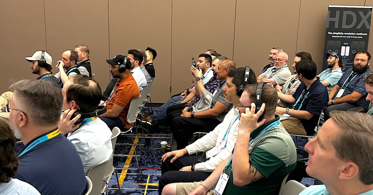 InfoComm attendees seated in rows and wearing headphones during a live HDX full-featured audio demonstration, listening to an Auracast broadcast audio demo.