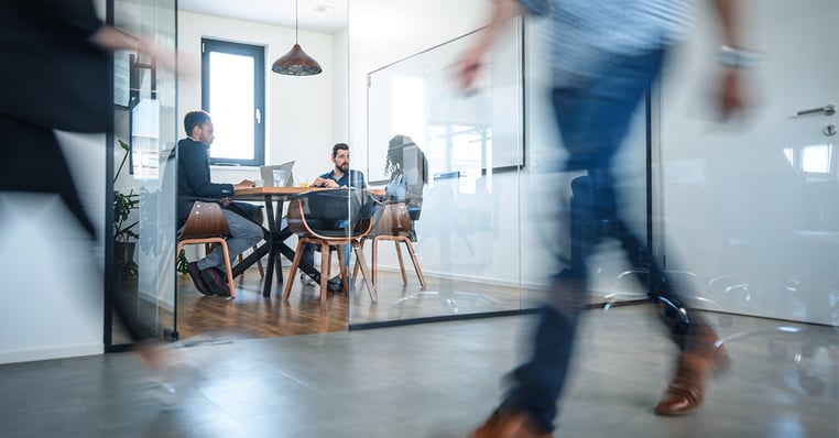A person walks by a hybrid meeting happening in a small space