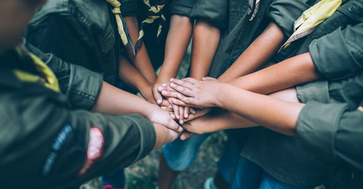 Image of five Scouts in uniform putting their hands together. 