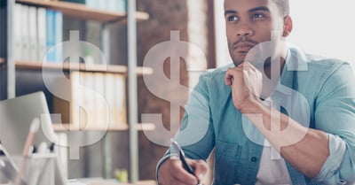 Man sits in front of a computer with pen in hand. Dollar signs are placed on top of the image.