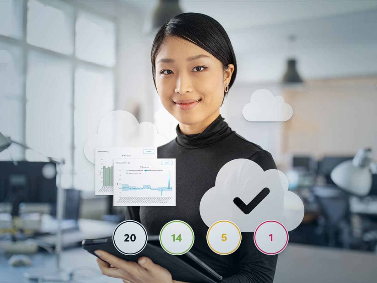 IT professional holding a tablet with Nureva Console graphics showing room status indicators, usage data and background noise charts.