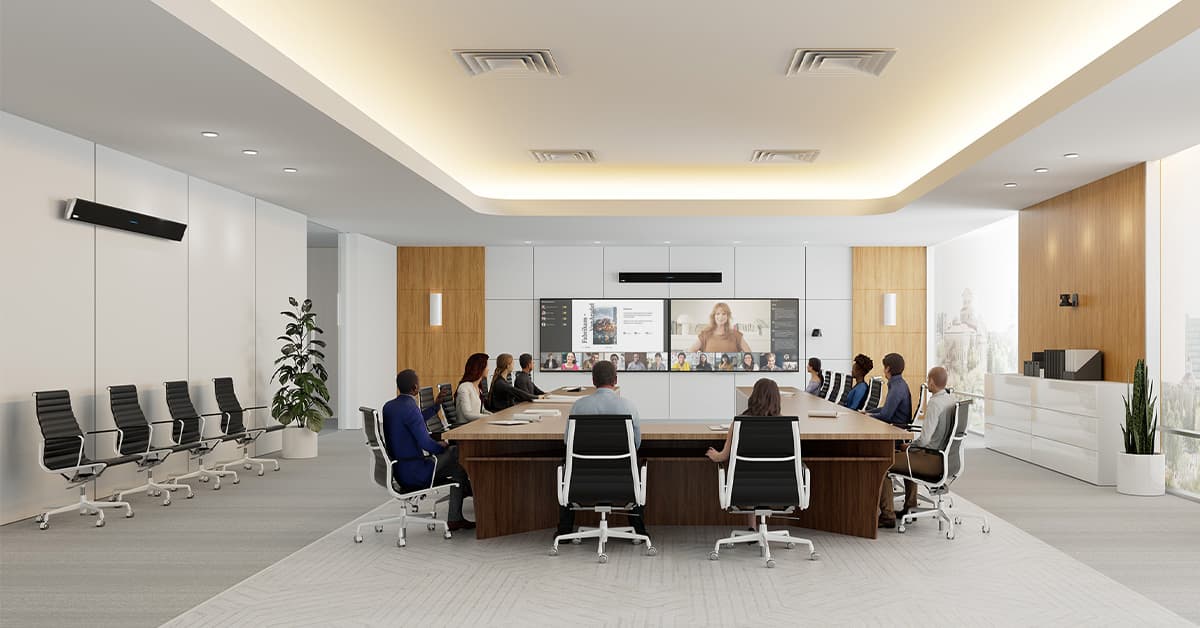 Executive meeting room with people featuring Nureva HDL410 microphone and speaker bars mounted on the wall, with a large conference table, modern chairs and display screen.