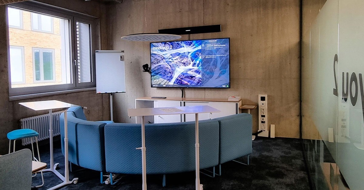 Cubex 41 modern meeting space with curved blue seating, a large wall-mounted display and a Nureva HDL audio bar installed above for hybrid collaboration.
