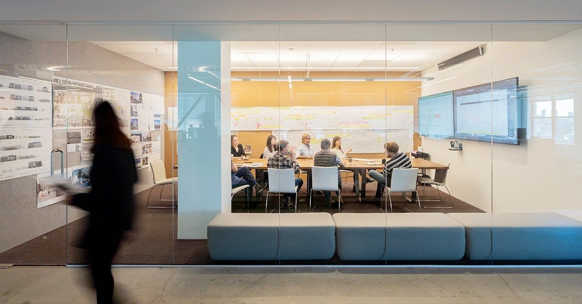 WRNS Studio modern glass-walled meeting room with team members collaborating around a conference table, equipped with Nureva audio conferencing for hybrid meetings.