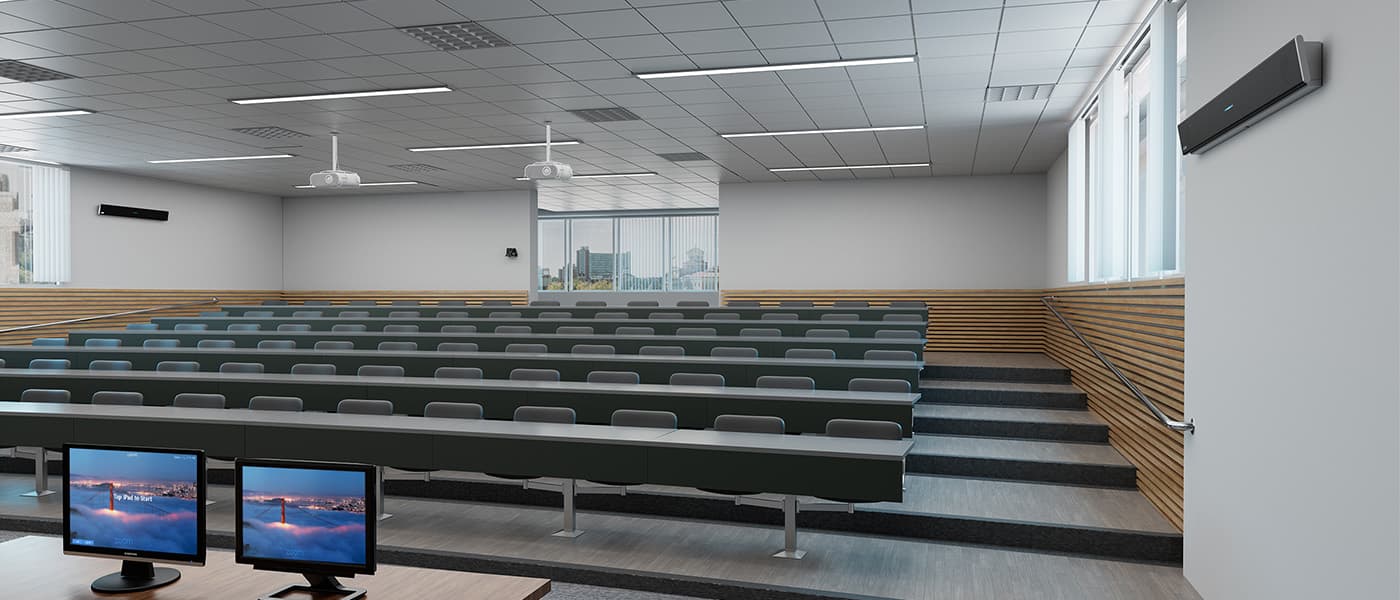 Large tiered lecture hall configured as a Zoom Room, featuring a Zoom-certified Nureva HDL410 audio conferencing system mounted on the right side wall, stepped rows of fixed seating, two ceiling-mounted projectors and dual instructor monitors at the front desk showing the Zoom Rooms idle screen.
