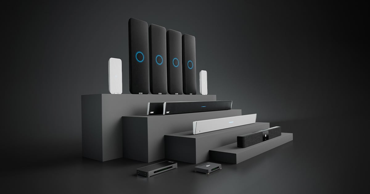 Nureva audio products on a tiered display fixture arranged by room size and use case, from audio conferencing in medium meeting rooms to full-featured audio in extra-large classrooms and boardrooms.