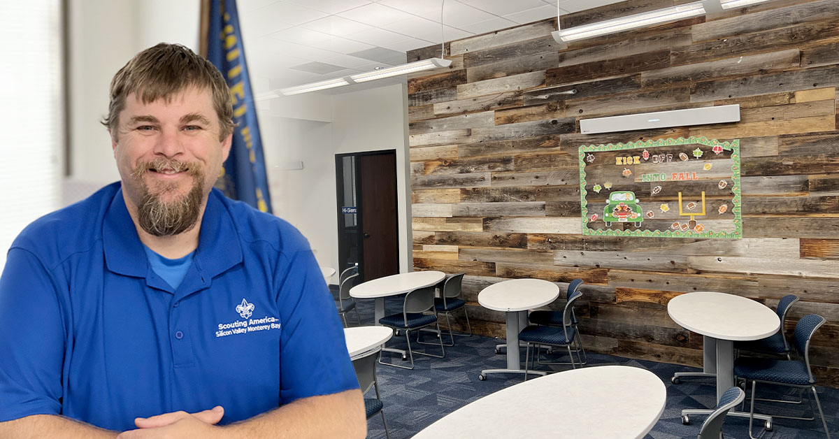 Michael Wilson, COO of the Silicon Valley Monterey Bay Council of Scouting America, stands in front of a multipurpose room with several tables and chairs and a Nureva microphone and speaker bar.