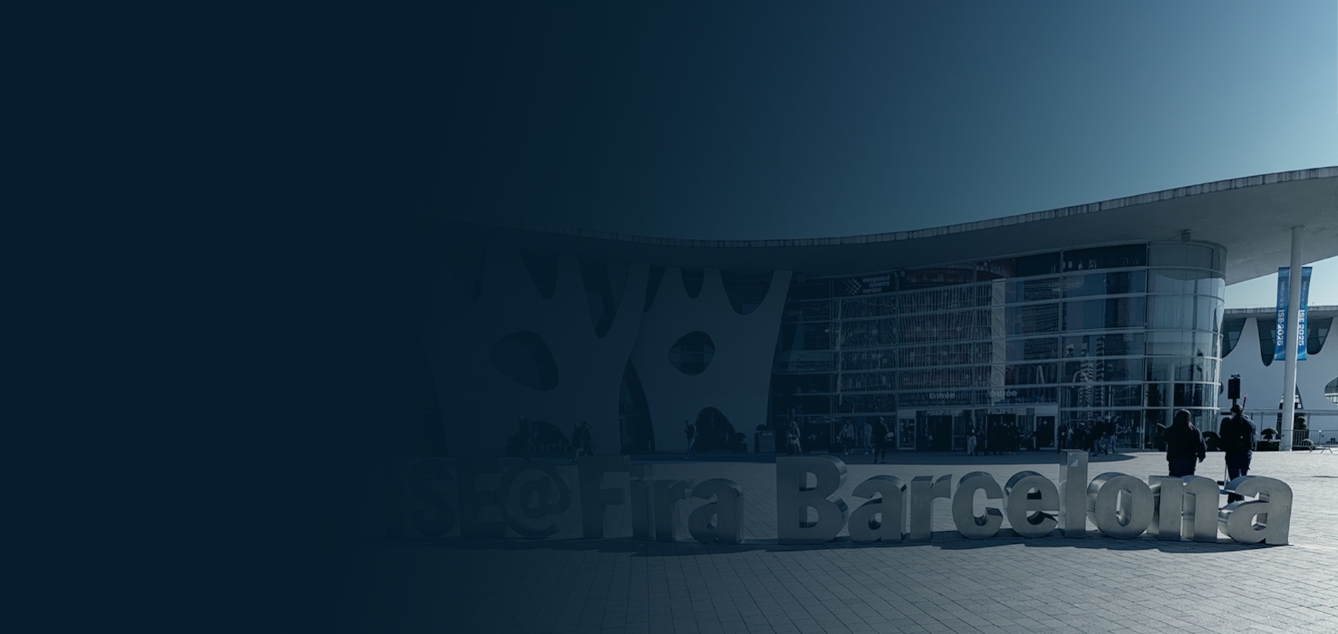 Exterior view of Fira Barcelona Gran Via during ISE conference, featuring modern architecture with white sculptural facade and large glass entrance, plus prominent ISE@Fira Barcelona signage in the foreground.