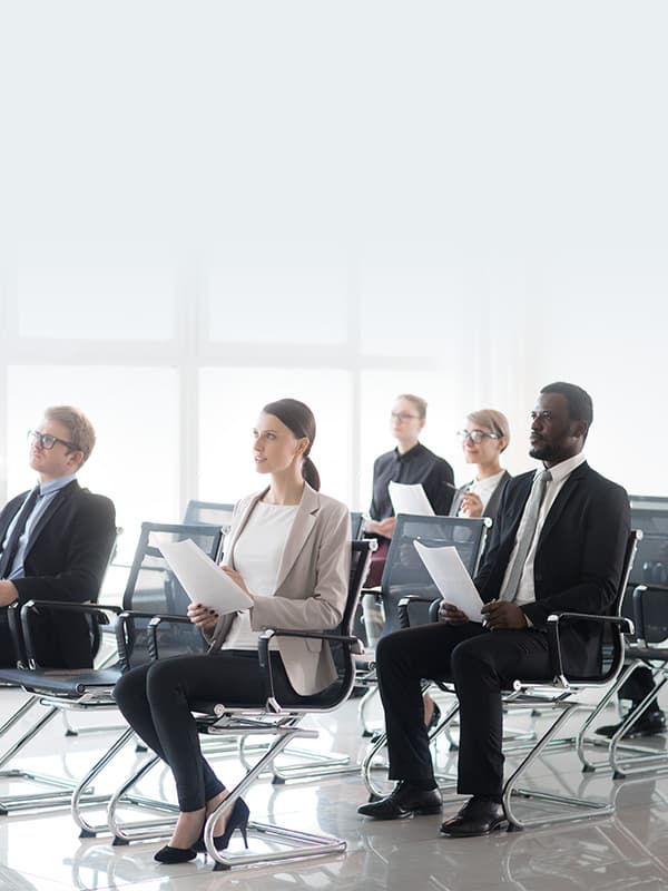 Government professionals seated in a bright training room holding documents and listening attentively during a public sector learning session.