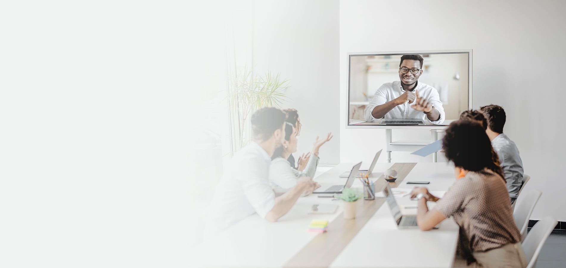Small business team seated at a conference table engaging with a remote participant displayed on a wall-mounted screen during a hybrid meeting.