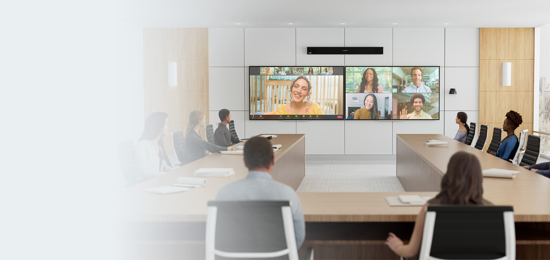Zoom Room featuring a Zoom-certified Nureva HDL310 audio conferencing system mounted above dual wall-displays, with in-person participants seated at parallel meeting tables collaborating with remote colleagues shown in gallery view on the front-of-room Zoom video conference screens.